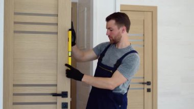 Ahşap iç kapının montajı. Üniformalı kapılı genç çilingir portresi. Profesyonel tamir servisi. Bakım Kavramı.