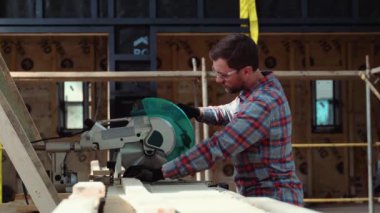 İnşaatçı tahta keserken dairesel testereyle tahtayı testereyle kesiyor..