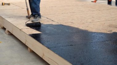 Applying hot resin to the floor for waterproofing, roller and bucket of resin, black and liquid resin.