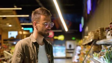 Genç adam bakkalda alışveriş yapıyor. Alışveriş sepetleri tutan ve markette taze meyve ve sebze seçen kadın ve erkeğin yan görüntüsü. Alışveriş konsepti