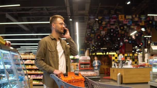 Молодой Человек Супермаркете Разговаривает Телефону Консультируется Своей Женой Списке Покупок — стоковое видео