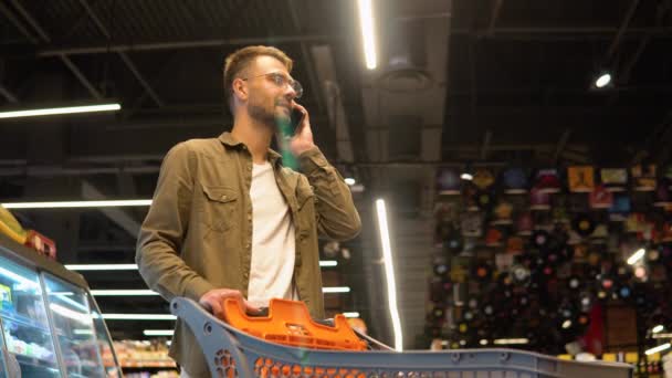 Молодой Человек Тролли Супермаркете Разговаривает Телефону Консультируется Своей Женой Списке — стоковое видео
