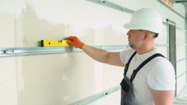 Bir adam alçı duvarın yatay sapmasını ölçer..