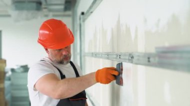 Üniformalı bir işçi alçıpan duvarına alçı yapıştırıyor. Alçı levha eklemlerinin macunu.