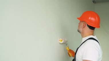 Ressam boya silindiri tutuyor ve bir duvar boyuyor. Yeni evdeki boya silindiriyle iç duvar boyama..