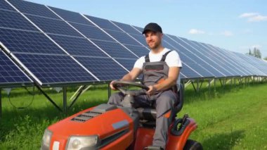 Güneş panelleri istasyonunda çim biçme makinesiyle çim biçen bir işçi.