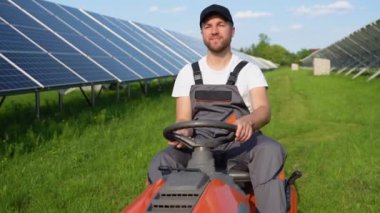 Bir adam güneş panellerinin yakınındaki çimleri biçiyor. Yeşil enerji.