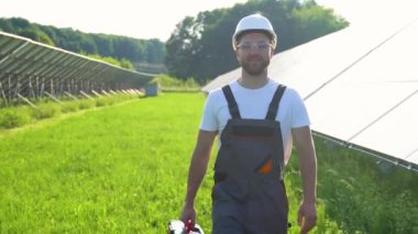Koruyucu iş giyimi mühendisi olan güneş enerjisi santrali fotovoltaik panelleri inceliyor ve yürüyor. Alternatif enerji kavramı ve onun bakımı.