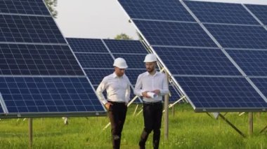 Güneş çiftliği ve iki mühendis sistemin işleyişini kontrol etmek için yürüyorlar. Dünyanın enerjisini korumak için alternatif enerji. Temiz enerji üretimi için fotovoltaik modül fikri.