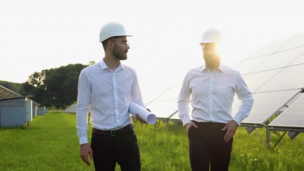工程师在太阳能农场散步 讨论有效的建设计划 两个头戴防护头盔 身穿制服的男人在说话 替代能源的概念 — 图库视频影像