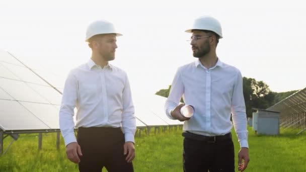工程师在太阳能农场散步 讨论有效的建设计划 两个头戴防护头盔 身穿制服的男人在说话 替代能源的概念 — 图库视频影像