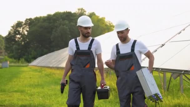 太阳能发电厂由两名穿着防护服的工程师组成 他们带着工具行走和检查光伏面板 替代能源的概念及其维护 — 图库视频影像