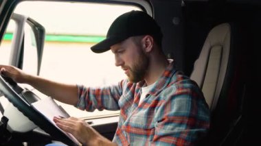 Kamyonda karton kutu kontrol listesi olan teslimatçı. Panodaki kurye kontrol listesi. Teslimatçı kamyonda oturuyor ve teslimat listesini kontrol ediyor..