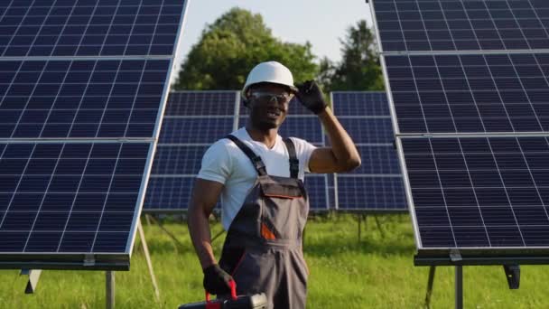 英俊的非洲男性技师 身穿制服 站在一排太阳能电池板前 手持工具 看着相机 — 图库视频影像