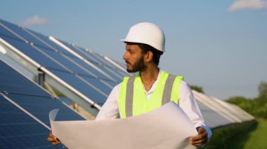 Koruyucu miğferli Hintli teknoloji uzmanının portresi. Güneş panelleri yerleştiren kağıt planına bakan işadamı.