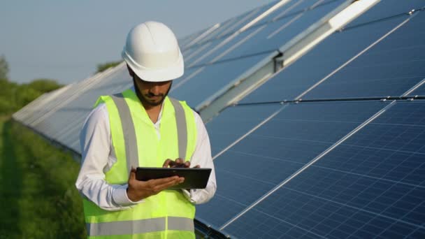 年轻的印度工程师站在蓝天明亮的太阳能电池板旁边 研究平板电脑 可再生能源 绿色能源和清洁能源 复制空间 工作上的工人 印度技能A — 图库视频影像