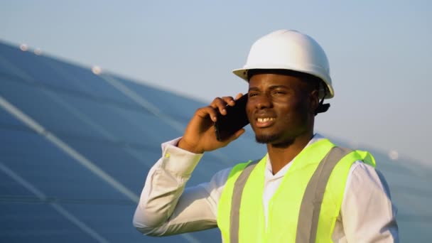 Африканский Американский Электрик Жилете Шлеме Разговаривает Телефону Стоит Фоне Солнечных — стоковое видео