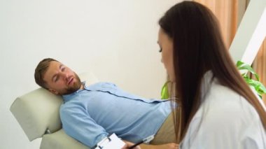Kadın profesyonel psikolog, ofisinde oturan stresli erkek hastaya bir konsültasyon yapıyor. O bir kağıda yazıyor. Psikolojik danışman konsepti.