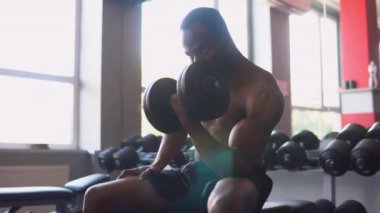 Kaslı siyah adam spor salonunda çalışıyor. Alternatif olarak ağır halterleri kaldırıyor ve kasları için egzersiz yapıyor..