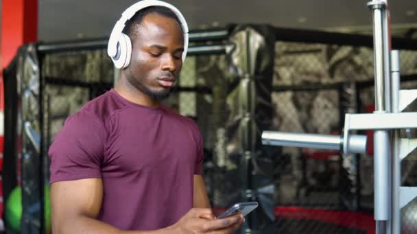 Zmęczony Czarny Kulturysta Siedzi Siłowni Słucha Muzyki Używa Telefonu Komórkowego — Wideo stockowe