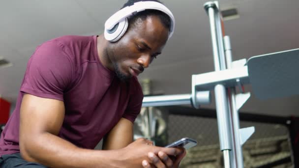 Bodybuilder Nero Stanco Seduto Palestra Ascoltando Musica Utilizzando Telefono Cellulare — Video Stock