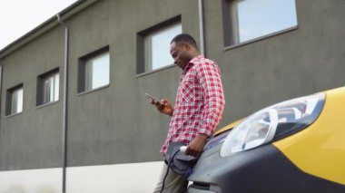 Elektrikli araç şarj istasyonunda akıllı telefon tutan siyah bir adam var..