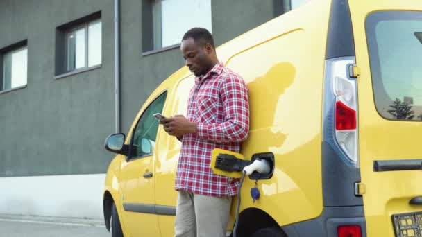 Homem Preto Segurando Smartphone Enquanto Carrega Carro Caminhão Estação Carregamento — Vídeo de Stock