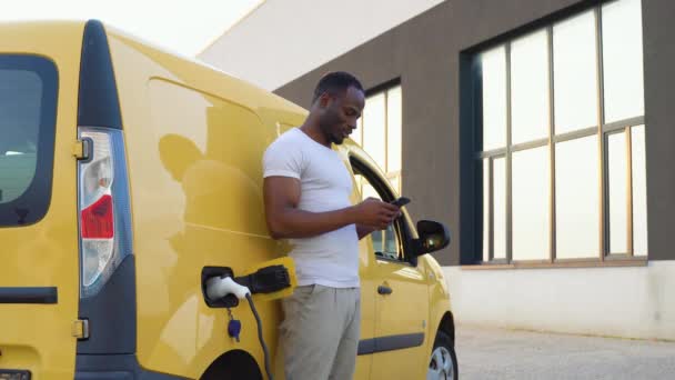 African American Man Chatting Mobile Phone While Electric Car Charging — Stock Video