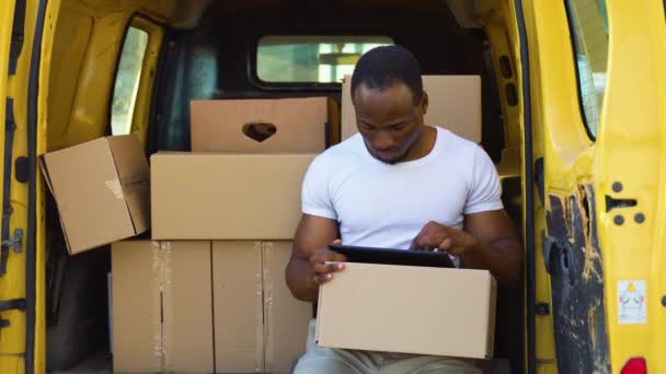 Αφρικανός Γοητευτικός Ντελιβεράς Κάθεται Στο Φορτηγάκι Γεμάτος Δέματα Έναν Υπολογιστή — Αρχείο Βίντεο