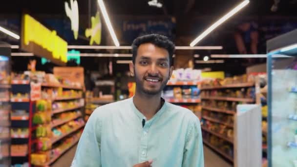 笑顔のインドの男は スーパーマーケットで彼のトロリーと通路を歩く — ストック動画