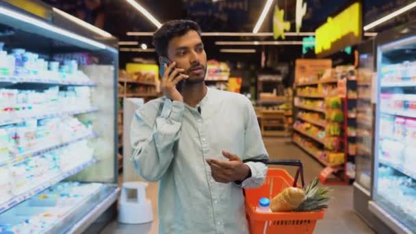 Индийский Мужчина Супермаркете Делает Покупки Выбирает Продукты Говорит Телефону Консультируется — стоковое видео