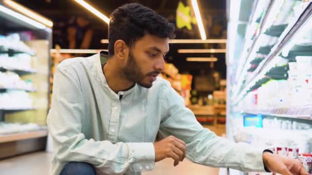 インド人男性が食料品店で乳製品を買い物している アイスクリームを買うハンサムな男のサイドビュー — ストック動画