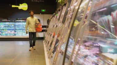 Gülümseyen Hintli adam süpermarkette trolleriyle koridorda yürüyor.