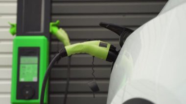 İstasyonda lüks beyaz elektrikli araba şarj edilir.