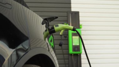 Tanınmayan siyah adam istasyonda şarj olan elektrikli aracın fişini çekti. Yeşil enerji, çevre dostu yakıt.