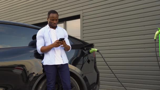 Чорношкірий Користується Телефоном Під Час Заряджання Електромобіля — стокове відео