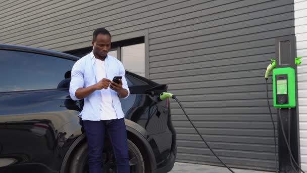 Чорношкірий Користується Телефоном Під Час Заряджання Електромобіля — стокове відео