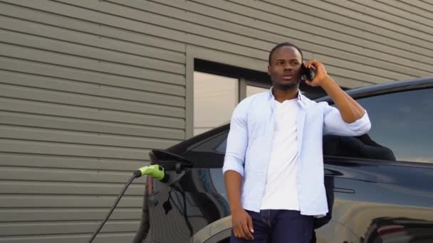 Şarj Istasyonunda Lüks Elektrikli Araba Şarj Ederken Siyahi Adam Telefonda — Stok video