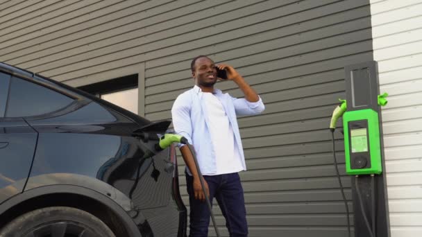 Hombre Afroamericano Hablando Por Teléfono Mientras Carga Coche Eléctrico Estación — Vídeo de stock