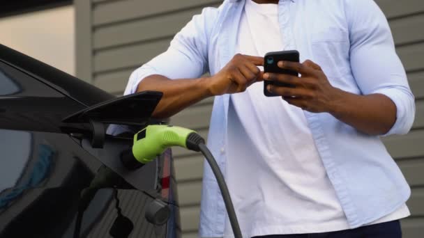 Чернокожий Мужчина Использует Мобильное Приложение Управления Аккумулятором Электромобиля — стоковое видео