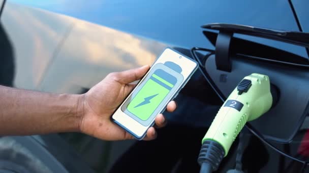 Svart Mann Bruker Mobilapplikasjon Kontrollere Batteriet Til Elektrisk Bil – stockvideo