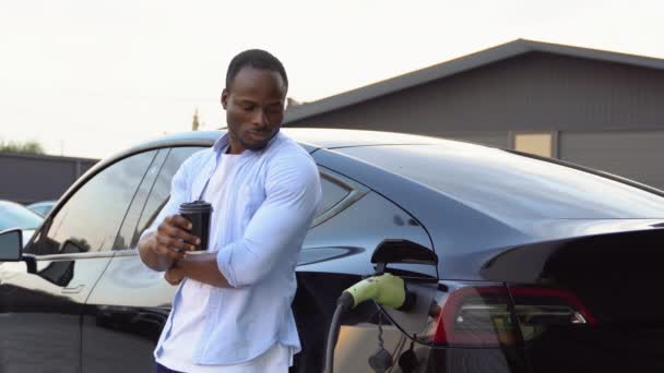 Siyah Adam Elektrikli Arabayı Şarj Ediyor Kahve Içiyor — Stok video