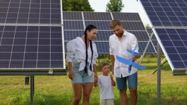 Güneşli bir günde, büyük bir güneş paneli çiftliğinin yakınlarında gezintiye çıkan neşeli üç kişilik aile.