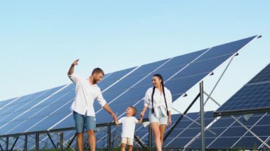 Güneşli bir günde, büyük bir güneş paneli çiftliğinin yakınlarında gezintiye çıkan neşeli üç kişilik aile.