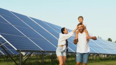 Güneşli bir günde, büyük bir güneş paneli çiftliğinin yakınlarında gezintiye çıkan neşeli üç kişilik aile..