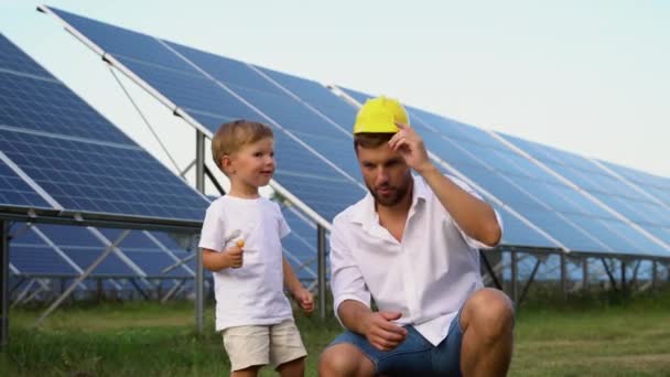 一个戴着孩子头盔的有趣的父亲和他的小儿子在太阳能电池板旁边 — 图库视频影像