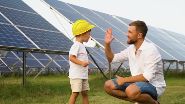 一个父亲和他的小儿子戴着黄色的头盔站在太阳能电池板旁边 — 图库视频影像