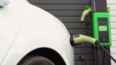 İstasyonda lüks beyaz elektrikli araba şarj edilir. Elektrikli arabalar, EV konsepti