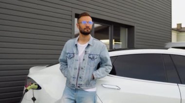 Elektrikli arabanın yanında bir adam, şarj istasyonunda şarj olmasını bekliyor..