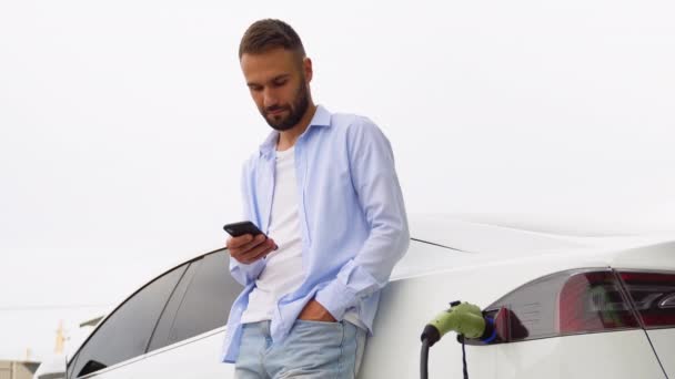 Vousatý Muž Používá Mobilní Aplikaci Ovládání Baterie Elektrického Auta — Stock video